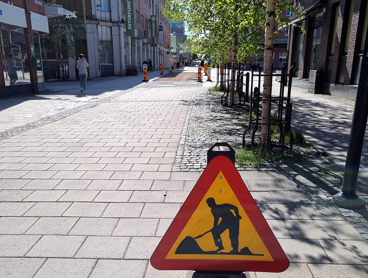 Skylt om pågående vägarbete med Köpmantorget i bakgrunden. Där har flera lösa plattor tagits bort i en rektangel
