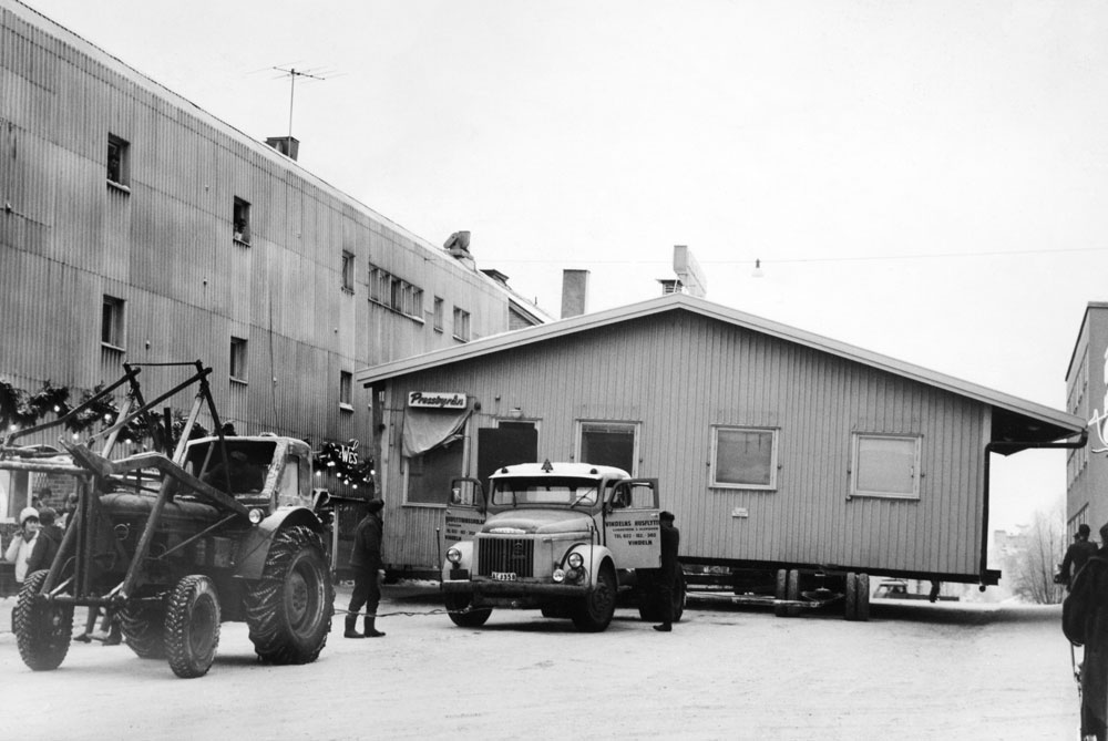 Traktor framför en lastbil som fraktar ett trähus som tar upp hela gatans bredd.